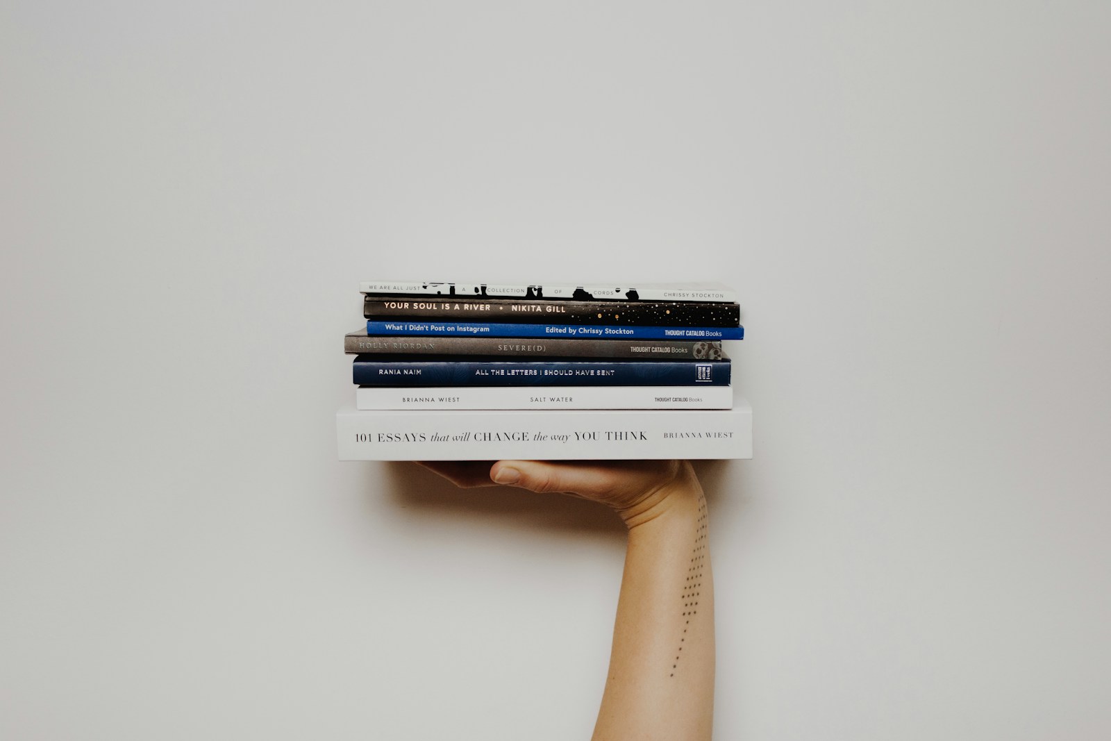 Eine Hand hält einen Stapel Bücher vor einer hellen Wand.